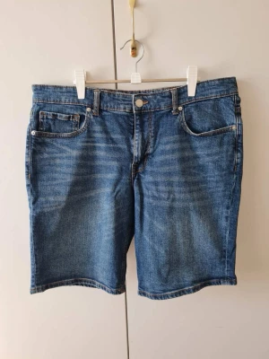 Cubus jeansshorts stl 36 blå herr - Blå jeansshorts från Cubus i normal passform, stl 36 (stretch). Klassisk femficksmodell med gylf och knapp framtill, i bomull med lite elastan.