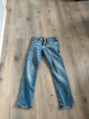 Blå jeans från supersey - Säljer ett par blå jeans med rak passform och klassisk femficksdesign. Jeansen har normal midja och subtila slitningar framtill för en avslappnad look. Perfekta för dig som gillar en tidlös stil och vill ha ett par jeans som funkar till det mesta.
