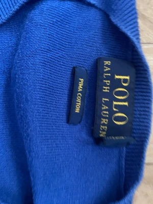 Blå stickad tröja Polo Ralph Lauren - Snygg blå stickad tröja från Polo Ralph Lauren i mjuk pima cotton. Tröjan har V-ringning och klassisk grön broderad logga på bröstet. Perfekt för dig som gillar stilrena och tidlösa plagg.