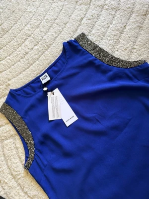 Blå ärmlös topp från Vero Moda - Snygg blå ärmlös topp från Vero Moda med glittriga detaljer längs axlarna. Perfekt för att lyfta din outfit med lite extra bling. Tunn och lätt i materialet, passar bra till både jeans och kjol.