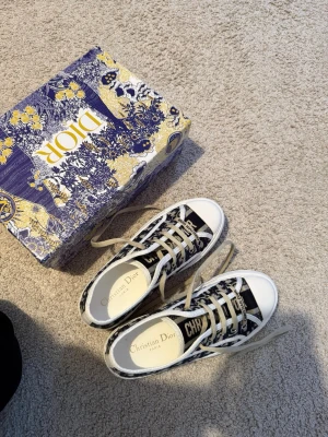 Christian Dior Oblique sneakers - Snygga låga sneakers från Christian Dior med klassiskt blått och vitt Oblique-mönster. Skorna har vita sulor, beige skosnören och tydlig Dior-logga på plösen. Perfekta för dig som vill sticka ut med exklusiv streetstyle.