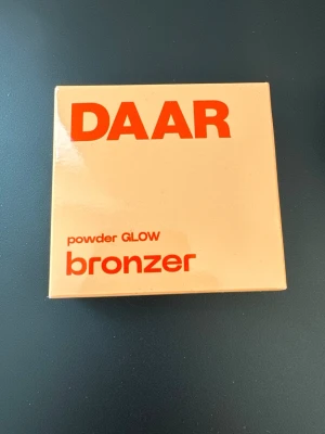 DAAR powder GLOW bronzer - Helt ny/oöppnad! DAAR puderbronzer i nyansen ”caramel cloud glow” (se bild 4, lånad bild). Produkten beskrivs som: En skimrig puderbronzer med en lätt och silkeslen formula som smälter in i huden och är enkel att blanda ut för ett vackert, naturligt resultat som håller hela dagen. Pigmentet kan byggas upp från subtilt glow till mer intensivt bronzat resultat, så att du kan skapa precis det resultat du vill ha.