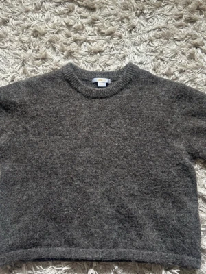 Mörkgrå stickad tröja Gina Tricot - Mysig mörkgrå stickad tröja från Gina Tricot med rund halsringning och rak passform. Perfekt för lager-på-lager och enkel att matcha med jeans eller kjol. Tröjan har en klassisk look och är gjord i ett mjukt, fluffigt material.
