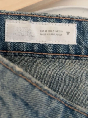 Ljusblå ripped jeans från ZARA - Säljer ett par ljusblå jeans från ZARA i storlek 32. Jeansen har raka ben, slitningar och en stor ripped detalj på baksidan av ena benet. Klassisk femficksmodell och tillverkade i denim. Perfekta för en trendig och avslappnad look.