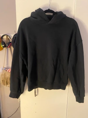 Svart hoodie med tryck 'Searching' - Svart hoodie med stor huva och tryck på ryggen som föreställer ett hus, träd och måne samt texten 'Searching' och 'Lightness From The Moon'. Oversized passform och ribbade muddar. 