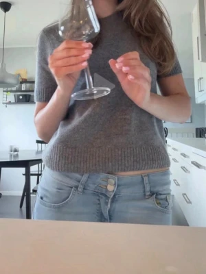 Grå stickad kortärmad tröja - Mysig grå stickad tröja med korta ärmar och rund hals. Tröjan har ribbade muddar vid ärmslut och nederkant, vilket ger en snygg och enkel look. Perfekt att matcha med jeans eller kjol för en chill stil. Endast använd en gång, fint skick. Nypris 400kr