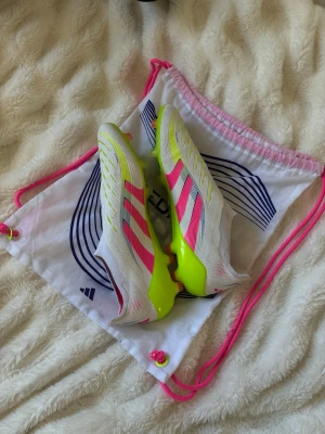Adidas vita och neonrosa fotbollsskor - Adidas predator nypris är 3199 skorna är använda ungefär 7 gånger så dom är fräscha dom sitter lite tajtare runt foten men de sitter skönt, de är storlek 45 1,3 så de är lite större en 45 men de är små i storleken, skriv om ni har några frågor💪färg (neon rosa vit och lime grön och små blå detaljer ( skorna är i elite) 
