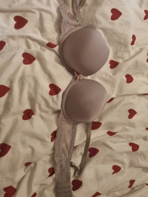 Ljusrosa push-up bh med spets - Säljer en ljusrosa push-up bh med vadderade kupor och fina spetsdetaljer längs sidorna. Bh:n har en liten rosett framtill och justerbara axelband. Perfekt för dig som vill ha både komfort och en snygg look.