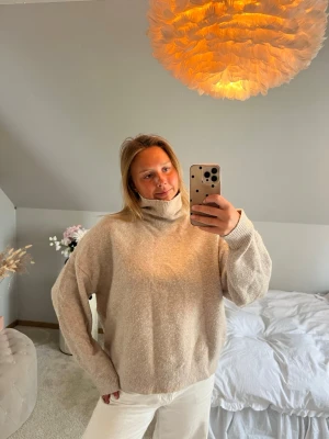 Beige stickad polotröja - Mysig beige stickad polotröja med avslappnad passform och ribbade muddar vid ärmslut och nederkant. Perfekt för lager-på-lager och enkel att matcha med olika outfits. Tröjan har en hög krage som ger extra värme.