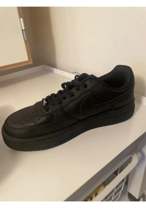 Svarta Nike Air Force 1 sneakers - Säljer ett par helsvarta Nike Air Force 1 sneakers med klassisk låg siluett. Skorna har snörning med metallbricka, perforerad tå och platt sula. Materialet är skinn och de har en rund tå. Snygga och tidlösa, perfekta för dig som gillar streetstyle. storlek men antar 39-40 