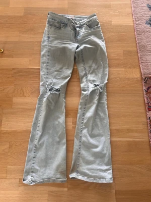 Ljusblå bootcut jeans  - Ljusblå bootcut jeans med slitna detaljer vid knäna och broderade bakfickor i rött. Klassisk femficksmodell med låg midja och utsvängda ben. Perfekta för en avslappnad och trendig look.