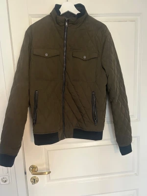 Olivgrön quiltad jacka med dragkedja - Snygg olivgrön quiltad jacka med svarta muddar och drakedja, storlek L men passar mig som bär S/M