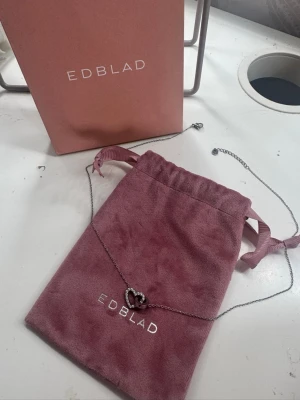 Halsband med hjärta från Edblad - Snyggt halsband från Edblad med ett silverfärgat hjärta och små pärldetaljer. Kedjan är tunn och elegant, perfekt för att lyfta vilken outfit som helst. Kommer med originalpåse och ask från Edblad.