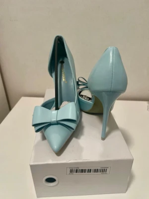 Ljusblå pumps med rosett - Snygga ljusblå pumps från Primadonna med spetsig tå och hög klack. Skorna har en stor dekorativ rosett framtill och är tillverkade i glansigt syntetmaterial. Perfekta för dig som vill sticka ut med en färgglad och trendig look.