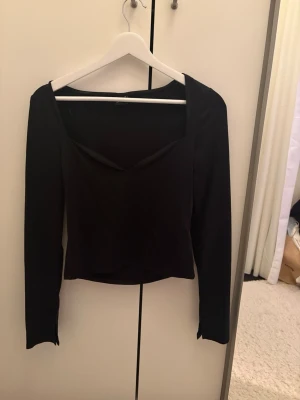 Svart långärmad topp Gina Tricot - Snygg svart långärmad topp från Gina Tricot med djupare v-ringning och figurnära passform. Perfekt att styla med jeans eller kjol för en trendig look. Enkel och stilren design som passar till många outfits.