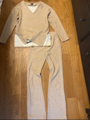 Beige loungewear-set från Amisu - Mysigt loungewear-set från Amisu i beige färg. Setet består av en långärmad tröja med v-ringning och matchande byxor med raka ben. Materialet är mjukt och stretchigt, perfekt för avslappnade dagar hemma.
