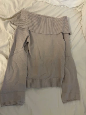 Beige off shoulder stickad tröja - Snygg beige stickad tröja med bred off shoulder-krage och långa ärmar. Tröjan har ribbstickade muddar vid ärmslut och nederkant, perfekt för en trendig och avslappnad look. Materialet känns mjukt och följsamt.