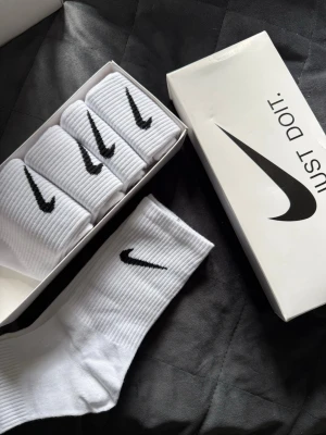 Vita Nike strumpor i 5-pack - Säljer ett 5-pack klassiska vita Nike strumpor med svart swoosh-logga. Strumporna är ribbade och har en sportig look som passar perfekt till sneakers. Tillverkade i mjuk och bekväm bomullsblandning.