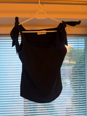 Mörkblå linnetopp med knytaxlar - Supersöt mörkblå linnetopp från Gina Tricot med knytbara axelband. Toppen har en enkel och stilren design, perfekt till jeans eller kjol. Tillverkad i mjuk bomull som känns skön mot huden.