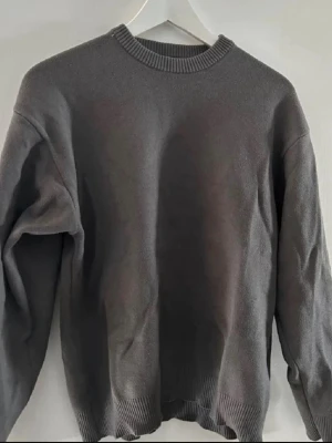 Mörkgrå stickad tröja  - En stilren mörkgrå sweatshirt med rund halsringning och ribbade muddar vid ärmslut och nederkant. Perfekt för en avslappnad look och enkel att matcha med andra plagg. Materialet känns mjukt och bekvämt.