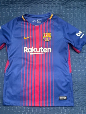 FC Barcelona Neymar Jr matchtröja barn storlek (Äkta köpt i Barcelona) - Säljer en officiell FC Barcelona matchtröja från Nike med Neymar Jr och nummer 11 på ryggen. Tröjan är blå med röda ränder, gula detaljer och klubbmärke på bröstet. Materialet är lätt och andas, perfekt för fotbollsträning eller att bära på läktaren.