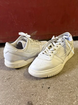 Vita Fila sneakers i - Stilrena vita sneakers från Fila i klassisk low-modell. Skorna är gjorda med diskreta detaljer och perforerad tå för extra ventilation. Perfekta för dig som gillar en clean och tidlös look. Snygga att matcha med både jeans och shorts.