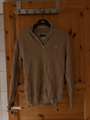 Beige halvzip-tröja från Gant - Snygg beige långärmad tröja från Gant med halv dragkedja och diskret logga på bröstet. Tröjan har en klassisk passform och är perfekt för lager-på-lager. Materialet känns mjukt och bekvämt mot huden.