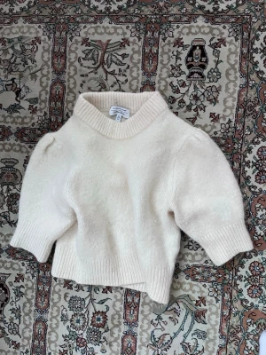 Krämvit stickad kortärmad tröja - Säljer en krämvit stickad tröja från Gina Tricot med korta puffärmar och hög ribbad krage. Tröjan är croppad och har breda ribbade muddar vid ärmslut och nederkant. Perfekt för en trendig och avslappnad look.