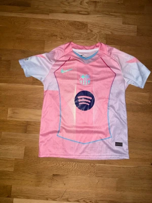 Barça rosa matchtröja Nike - Snygg rosa och ljuslila FC Barcelona matchtröja från Nike med tryck av Spotify-loggan och klubbmärke på bröstet. Nummer 10 och Lamine Yamal på ryggen samt Champions League-märke på ärmen. Perfekt för fotbollsfans som vill sticka ut.
