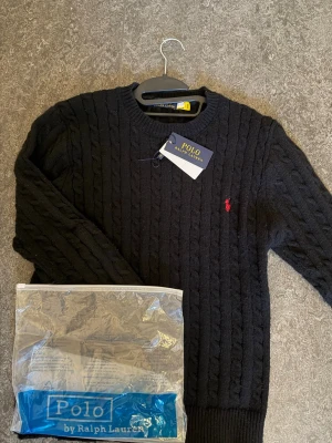 Svart kabelstickad tröja Polo Ralph Lauren - Kabelstickad tröja från Ralph lauren säljs i färgen svart, riktigt skön tröja med en helt sjuk passform på kroppen. Riktigt skön för layering och påse plus tags medföljer. Vid funderingar, skicka ett meddelande.