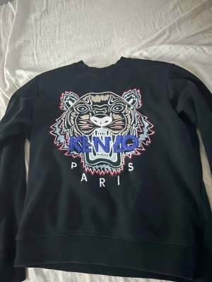 Svart Kenzo sweatshirt med tiger - Svart sweatshirt från Kenzo med ikoniskt broderat tigermotiv och färgglada detaljer framtill. Tröjan har rund halsringning och långa ärmar. Perfekt statement-plagg för dig som vill sticka ut.