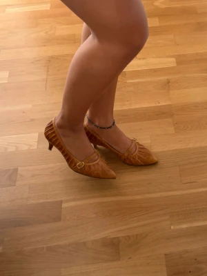 Bruna pumps  - Snygga bruna pumps från Ecco i skinn med spetsig tå och låg klack. Skorna har en dekorativ rem med spänne över foten och veckade detaljer längs sidorna. Perfekta för dig som gillar klassisk och stilren design. Skorna är köpta på aktion för 700kr  men blev aldrig använda då dem tyvärr var försmå. Skorna är i nyskick ser endast ut att vara använda fåtal gånger. Ända defekten på varan är ett jack i klacken baktill, men inget man tänker på🌸😍