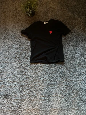 Svart Comme des Garçons Play t-shirt - Svart t-shirt från Comme des Garçons Play med det ikoniska röda hjärtat med ögon broderat på bröstet. Klassisk rund hals och korta ärmar. Tillverkad i mjuk bomull, perfekt för en clean och stilren look.