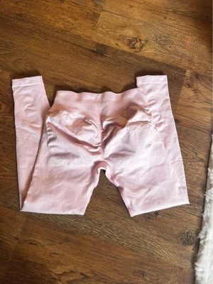 Ljusrosa scrunch-leggings från relode - Supersnygga ljusrosa leggings från relode med scrunch-detalj bak som framhäver formen. Hög midja och stretchigt material som sitter skönt. Perfekta för gymmet eller chill dagar. Diskret logga framtill i midjan. Storlek M i längden Regular men passar även s. Använd en gång