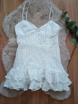  Ny treig Vit kort klänning med volang från Zara  - Söt vit kort klänning med smala axelband och volang nertill. Klänningen har broderade detaljer och är ärmlös, perfekt för varma dagar. Den har en feminin och luftig design som ger en fräsch sommarkänsla. Lånad bild 