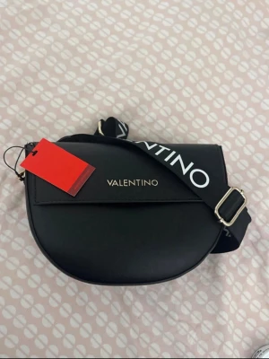Svart axelväska från Valentino - Snygg svart axelväska från Valentino. Fick väskan som present men den passade tyvärr inte med min stil så tänkte sälja den. Den är helt ny och oanvänd med taggen fortfarande på.