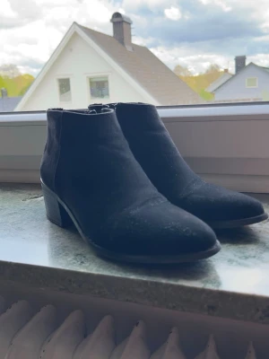Svarta Ankelboots / Boots med Klack – Strl 40 - Snygga svarta ankelboots med låg klack och stilren modell som passar både vardag och fest. Enkel att matcha med olika outfits och perfekt för höst/vår.  • Storlek: 40 • Färg: Svart • Dragkedja på sidan • Stabil och bekväm klack  Använda skor med normalt slitage. Det finns även synliga slitningar/märken på ena skon enligt bild, därav priset. Sulorna har fortfarande bra grepp kvar.  Se bilder för egen bedömning av skick.