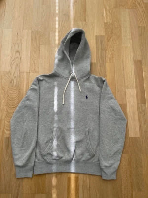 Grå hoodie från Polo Ralph Lauren - Snygg grå hoodie från Polo Ralph Lauren med klassisk blå logga broderad på bröstet. Fraktas samma dag som köp 😁 får med en överraskning i paketet, ställ frågor om ni har några 😄