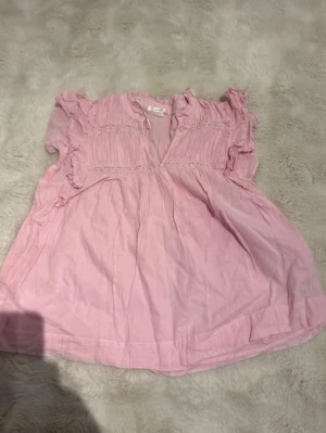 Rosa volangblus från Gina Tricot - Söt ljusrosa blus från Gina Tricot med volangdetaljer och rynk vid axlarna. Blusen har v-ringning och korta ärmar med volanger. Tillverkad i ett lätt och luftigt tyg, perfekt för en trendig look. Helt ny!!!❤️