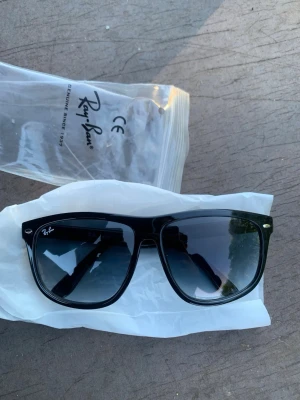 Svarta Wayfarer solglasögon Ray-Ban - Klassiska svarta Wayfarer solglasögon från Ray-Ban med bred båge och mörka glas. Snygg och tidlös design som passar till allt. Ray-Ban-logga på linsen och diskreta metalldetaljer vid fronten. Kommer i genomskinlig plastpåse.