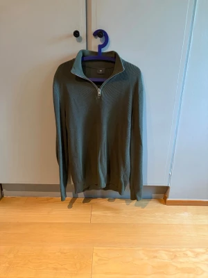 Olivgrön stickad tröja med dragkedja - Snygg olivgrön stickad tröja från H&M med halv dragkedja och hög krage. Tröjan har ribbstickad struktur och långa ärmar. Lappen är bortklippt men det är storlek S men större i storlek så passar M.