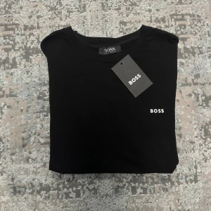 Svart  t-shirt - Snygg svart t-shirt med liten vit logga på bröstet. Klassisk rund hals och korta ärmar. Tillverkad i mjuk bomull som känns skön mot huden. Perfekt till jeans eller shorts för en clean och stilren look.