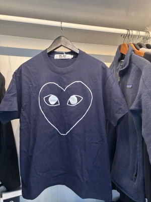 Blå Comme des Garçons Play t-shirt - Mörkblå t-shirt från Comme des Garçons Play med det ikoniska hjärtmotivet med ögon tryckt på bröstet. Klassisk passform med rund hals och korta ärmar. Perfekt för dig som gillar streetwear och vill sticka ut med en stilren look.