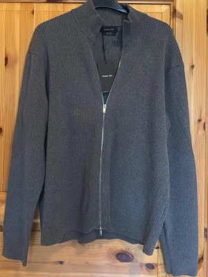 Massimo Dutti Cardigan - Mörkgrå ribbstickad ziptröja från Massimo Dutti med krage och hel dragkedja framtill. Tröjan har lång ärm och en stilren, minimalistisk design som passar perfekt till lager på lager. Helt ny och oanvänd, kvittot finns. Säljer pga passade inte min stil. Pris kan alltid diskuteras💫💫