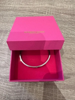 Silverfärgat armband Dyrberg/Kern - Stilrent armband i silverfärg från Dyrberg/Kern. Armbandet är runt och har en minimalistisk design, perfekt för dig som gillar enkla men snygga accessoarer. Levereras i original rosa ask med guldtext. Armbandet är 18 cm i omkrets och endast använd en gång!