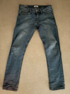 Blå slim fit jeans från Jack and Jones - Snygga blå slim fit jeans från H&M med klassisk femficksdesign och dragkedjegylf. Jeansen har en lätt tvättad look och smal passform som sitter tajt längs benen. Perfekta för en trendig och avslappnad stil. Storlek 30/30. ABS! Pris går att diskutera! Det finns ett hål mellan benen, därför är priset nersatt.