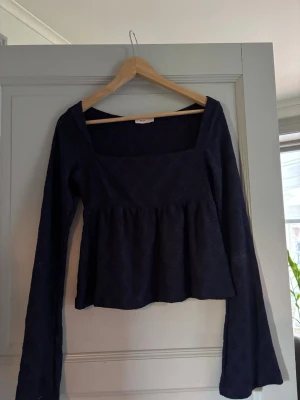 Mörkblå spetsblus från Nelly - Supersöt mörkblå blus från Nelly med lång ärm och fyrkantig ringning. Blusen har ett spetsmönster och lätt volang nedtill som ger en romantisk vibe. Perfekt att styla med jeans eller kjol för en trendig look.