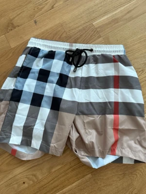  Burberry shorts  - Pris kan diskuteras vid snabb affär Säljer ett par klassiska rutiga shorts från Burberry med snörning i midjan. Shortsen har beige, svart, vit och röd färg i det ikoniska mönstret och är tillverkade i ett lätt syntetmaterial. Perfekta för sommaren och har en bakficka.
