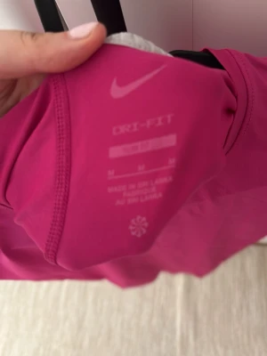 Rosa Nike Dri-Fit träningströja - Säljer en rosa Nike Dri-Fit träningströja i storlek M. Tröjan har korta ärmar och är tillverkad i ett snabbtorkande funktionsmaterial som passar perfekt till träning och sportaktiviteter. Klassisk Nike-logga framtill.
