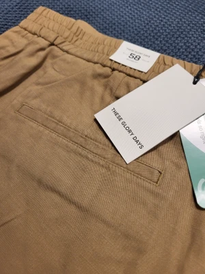 Beige shorts från These Glory Days 58 XXl - Stilrena beige shorts från These Glory Days med elastisk midja och diskreta fickor. Perfekta för en avslappnad look och tillverkade i mjuk bomull som känns skön mot huden.